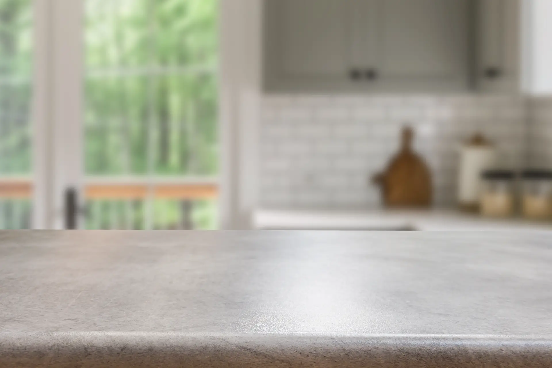 Nahaufnahme einer leeren, sauberen Arbeitsplatte aus grauem Stein mit verschwommener Küche im Hintergrund – Tipps für das richtige Reinigen der Küchenarbeitsplatte.