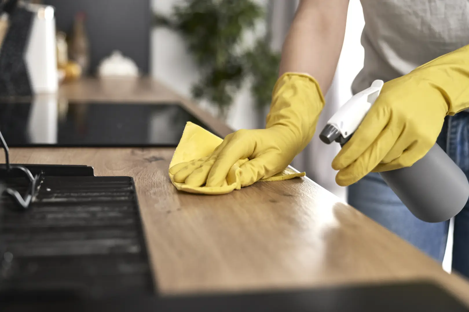 Eine Frau putzt mit gelben Gummihandschuhen und einem Mikrofasertuch die matten Fronten von beigefarbenen Küchenschränken, passend zum Thema matte Küchenfront putzen.