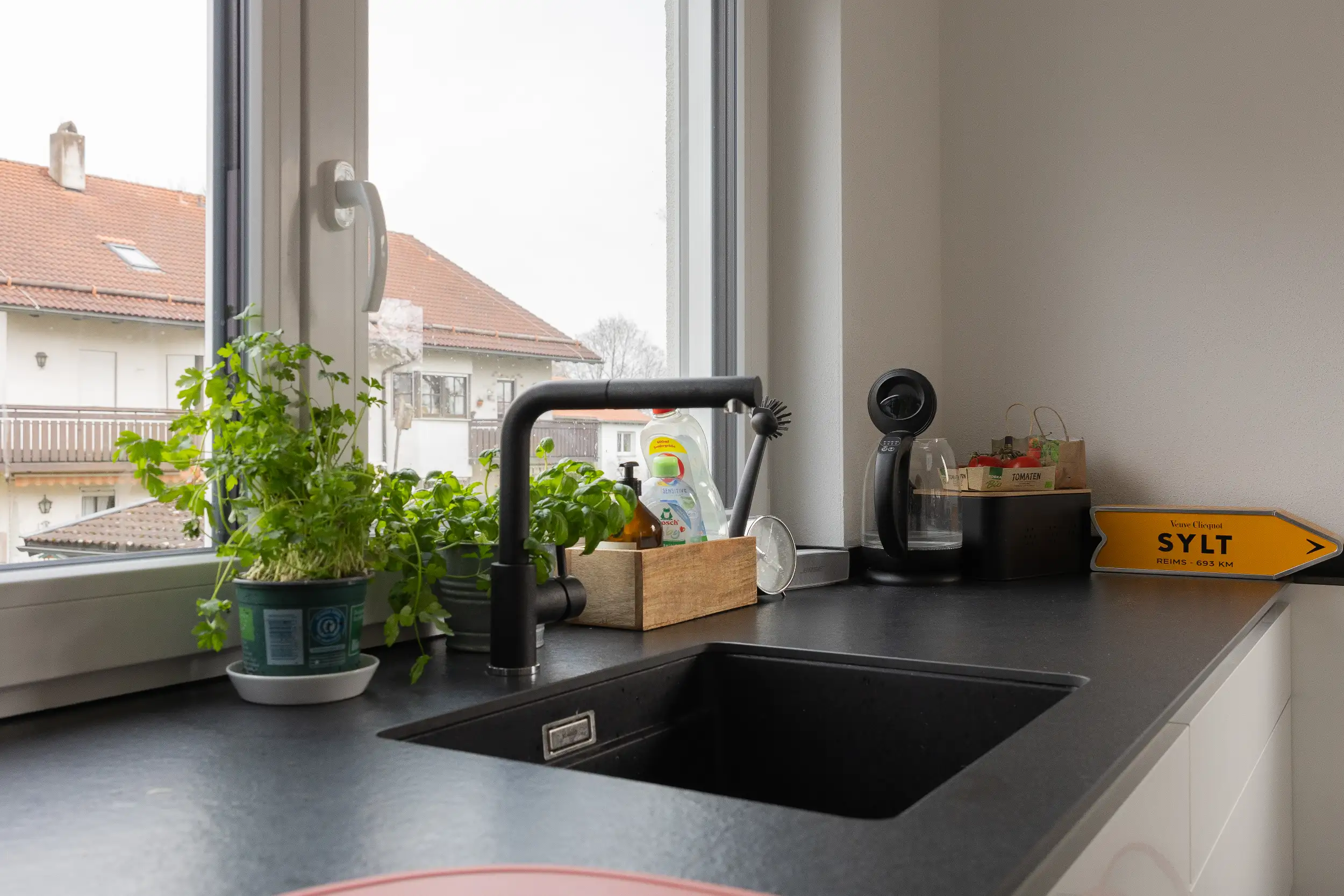 Praktischer Spülenbereich mit Blick in den Garten. Die moderne weiße Nolte Küche nutzt das Tageslich perfekt. Die schwarze Spüle samt Armatur mit einem Schwenkbereich von 360° ist funktional und stilvoll zugleich.