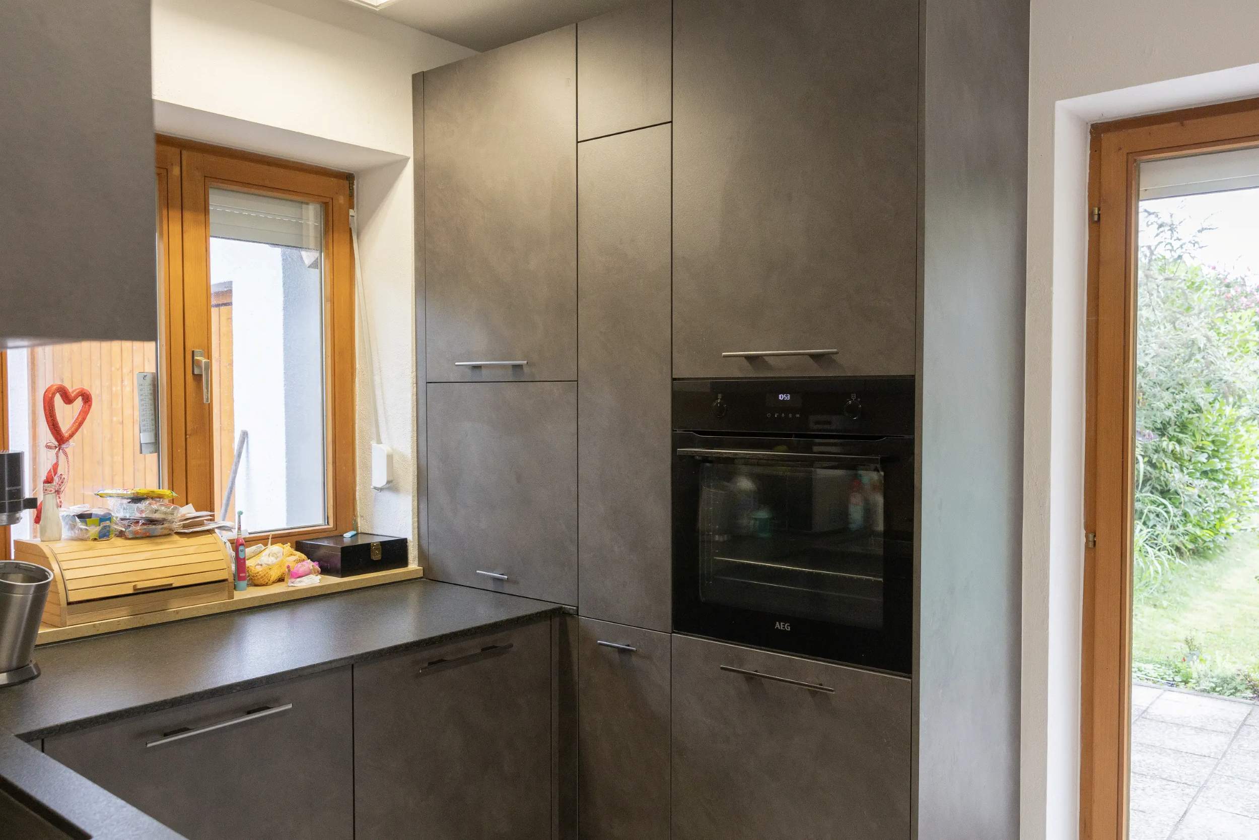 Moderne, maßgeschneiderte Küche mit matten Fronten in Betonoptik, ausgestattet mit einem AEG Einbau-Backofen. Perfekt für stilvolles und funktionales Kochen. Die harmonische Kombination aus ergonomischem Design und hochwertigen Materialien bietet maximalen Stauraum und Effizienz in einer kompakten Küchenumgebung. Ideal für kleine Räume, um modernes Küchenleben zu genießen
