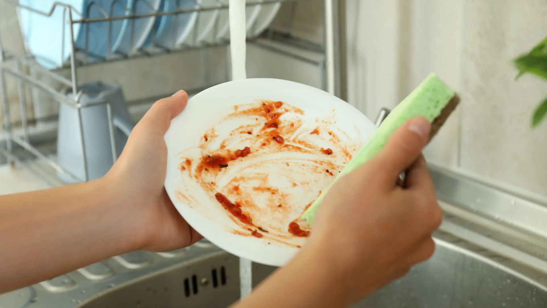 Nahaufnahme der Hände, die einen schmutzigen Teller unter fließendem Wasser vorspülen.