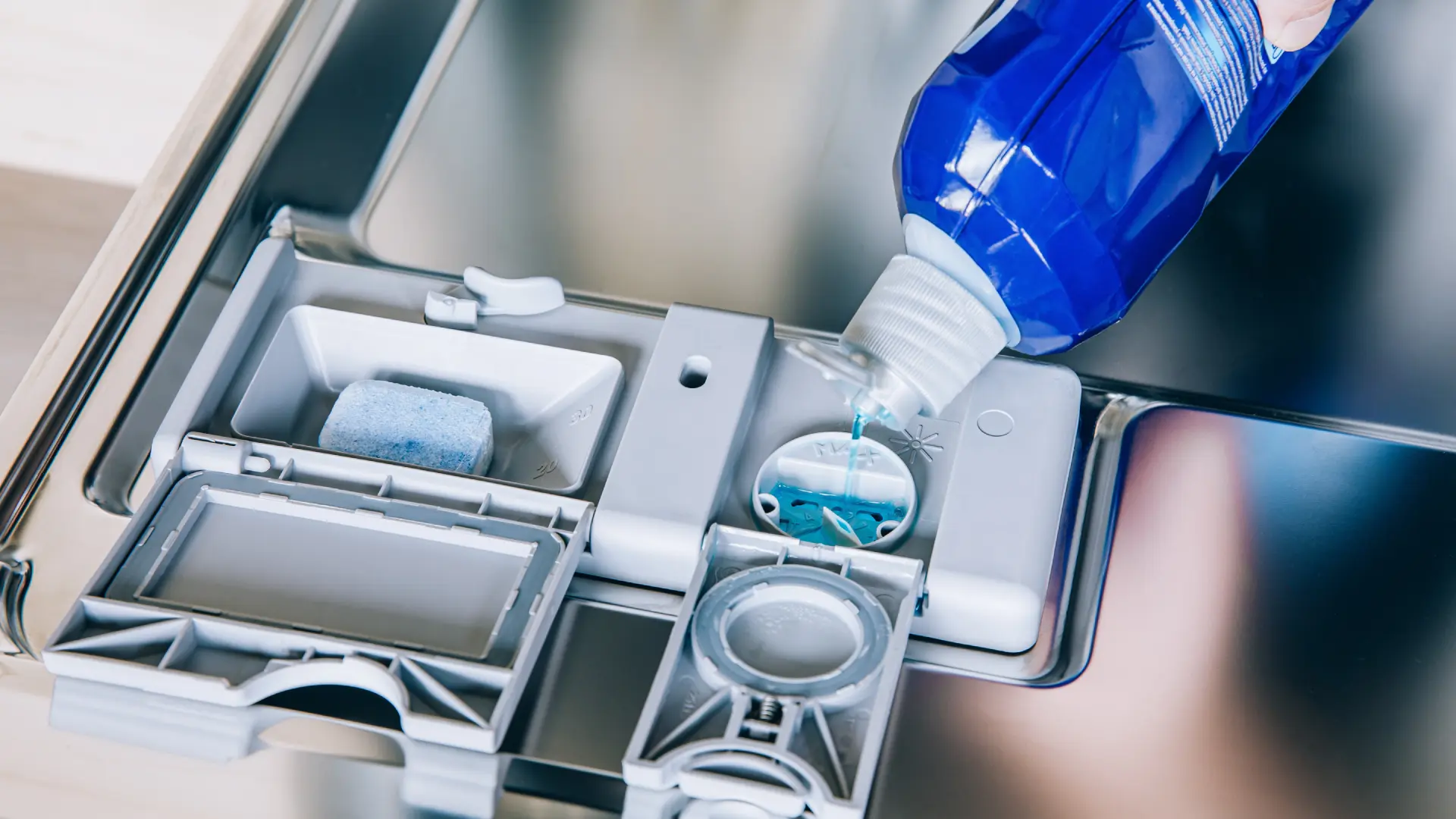 Klarspüler wird aus einer blauen Flasche in das Dosierfach des Geschirrspülers gefüllt.