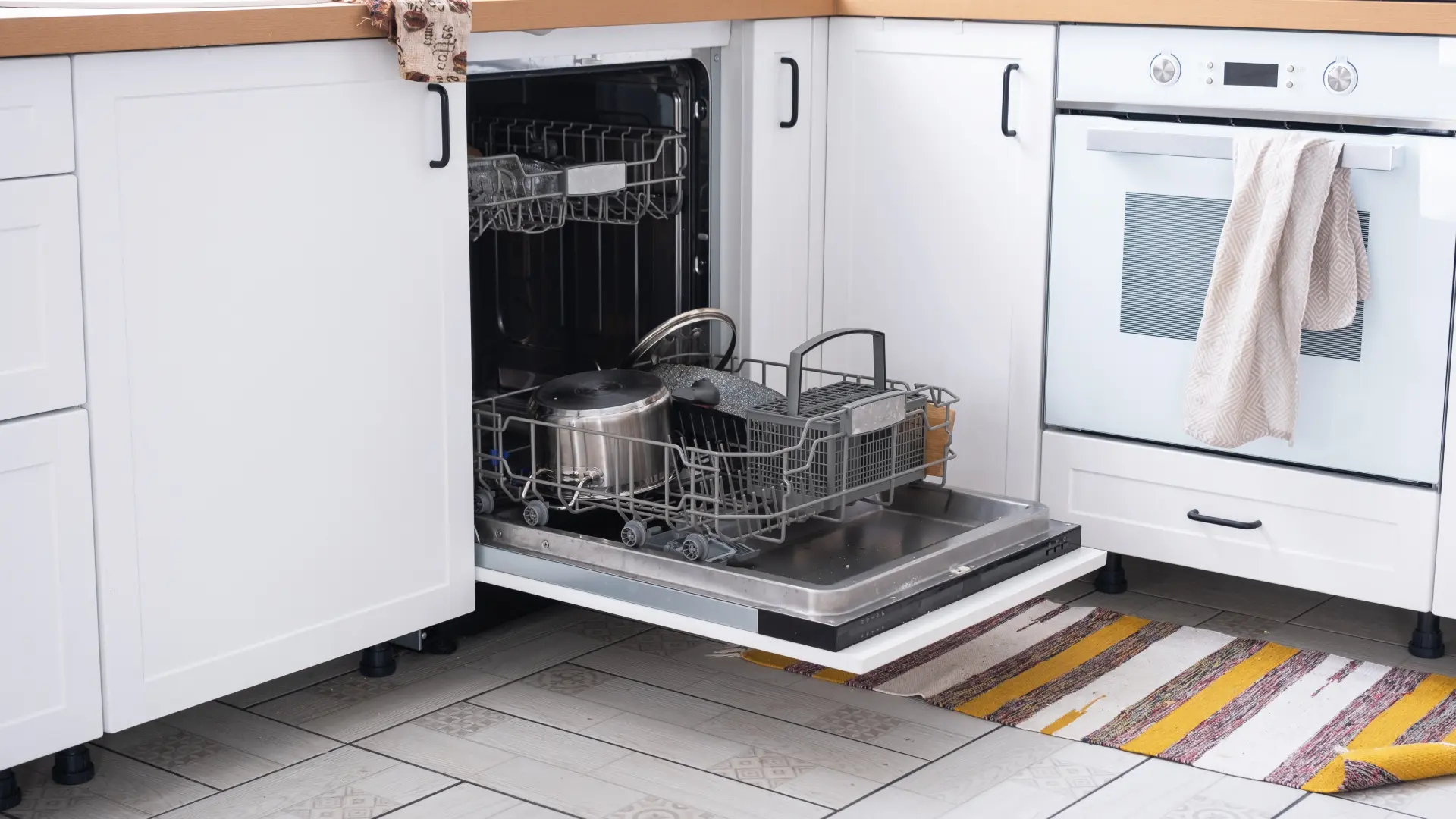 Offener, voll beladener Geschirrspüler in einer modernen weißen Küche.