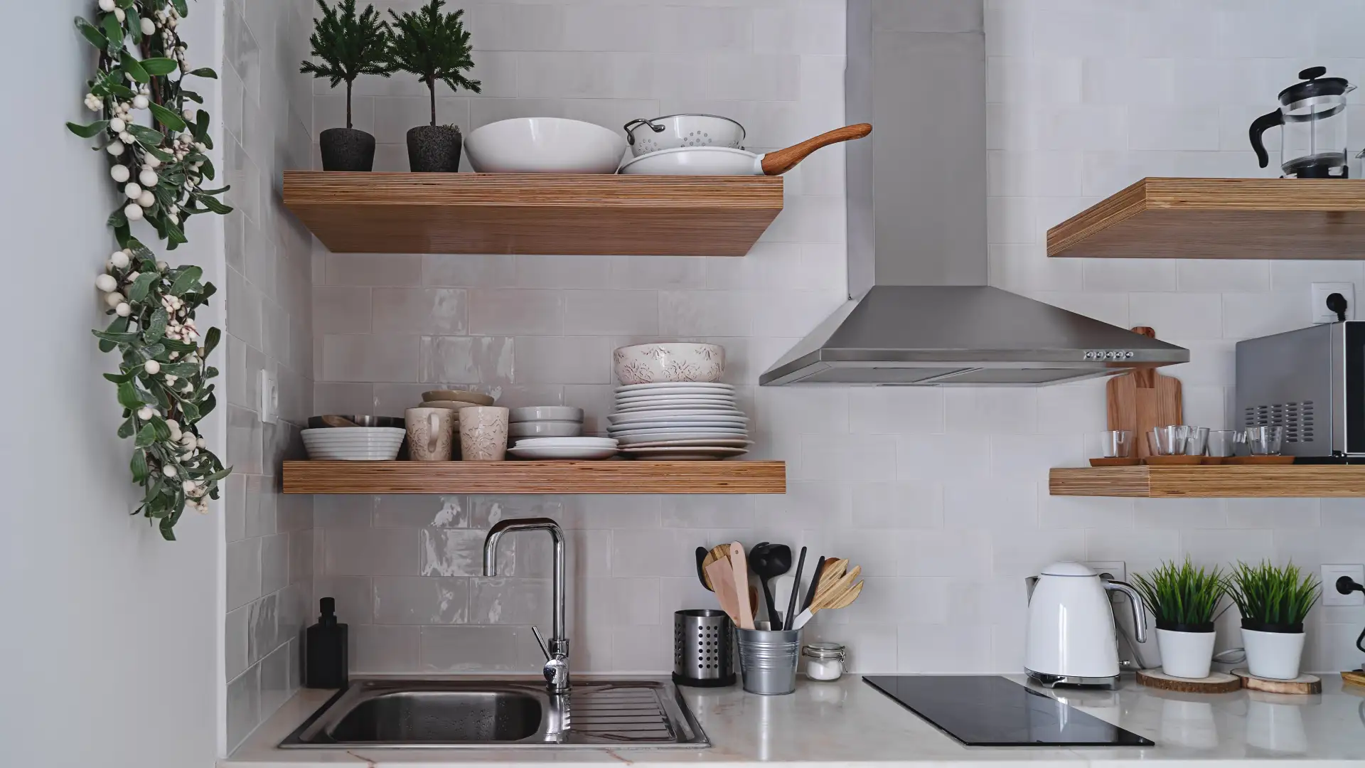 Kleine moderne Küche mit weißen Fliesen und Hochregalen aus Holz, auf denen Teller, Pfannen und eine Mikrowelle stehen