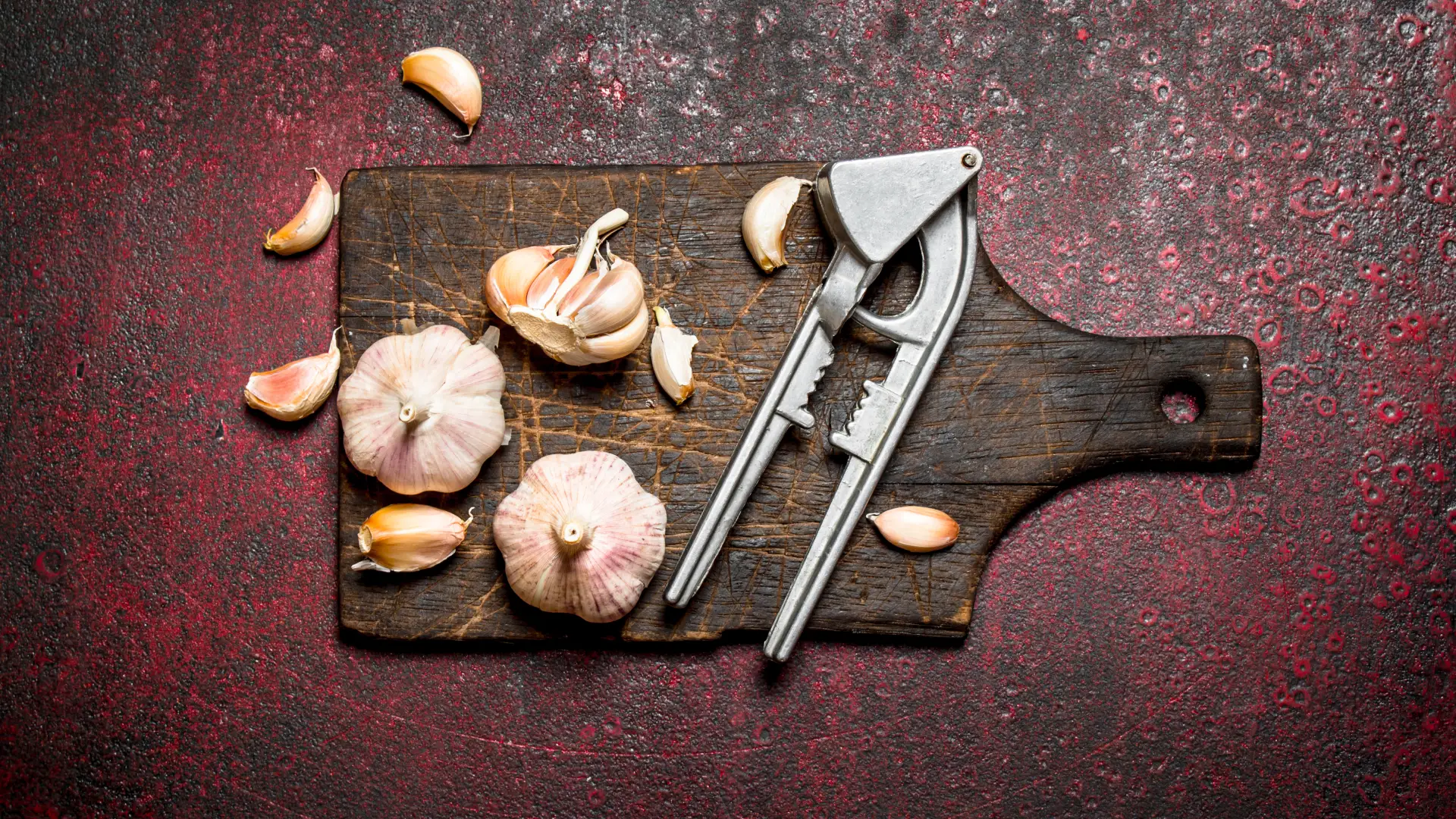 Robuste Knoblauchpresse aus Metall und frische Zehen auf dunklem Holzbrett