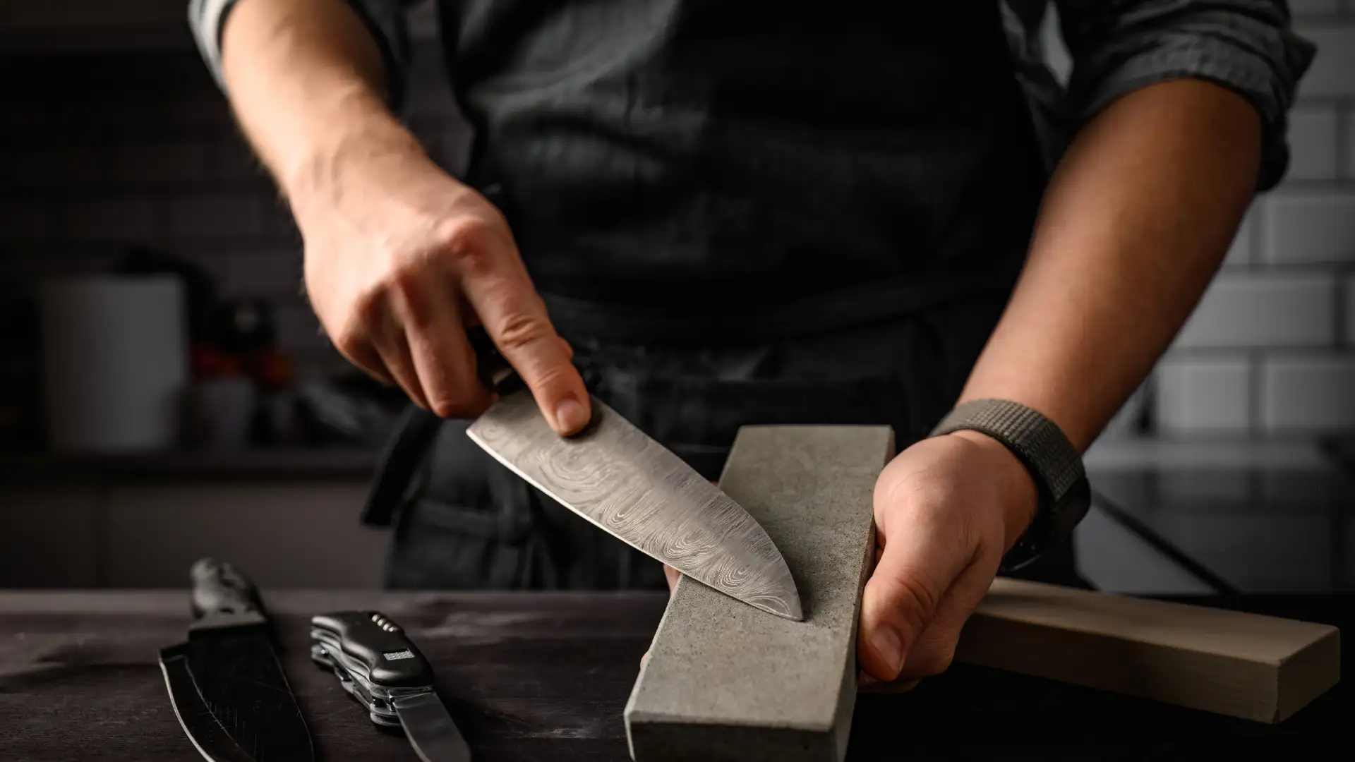 Koch schärft professionell ein Damastmesser manuell auf einem Schleifstein