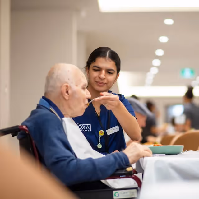 Staff member helping an elderly resident eat a meal