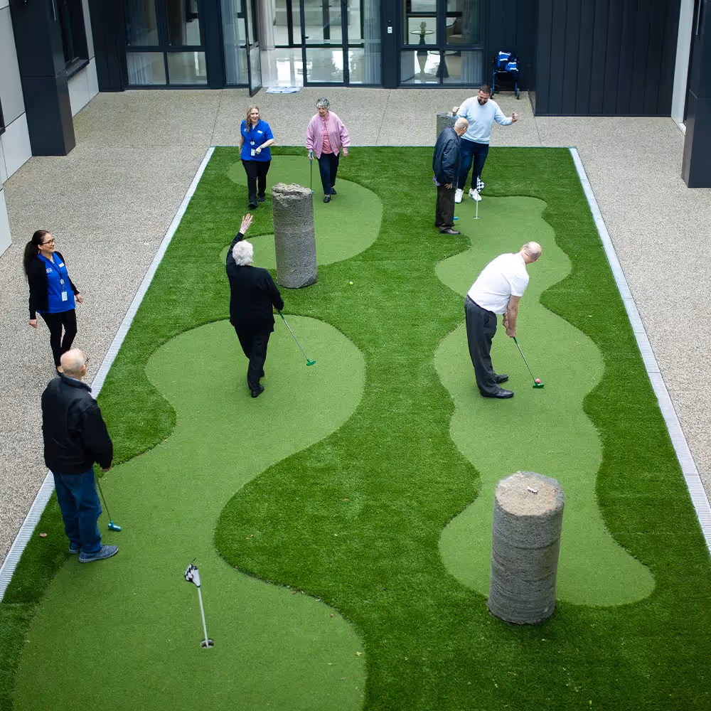Residents at South Morang aged care facility playing mini golf in landscaped garden courtyard.