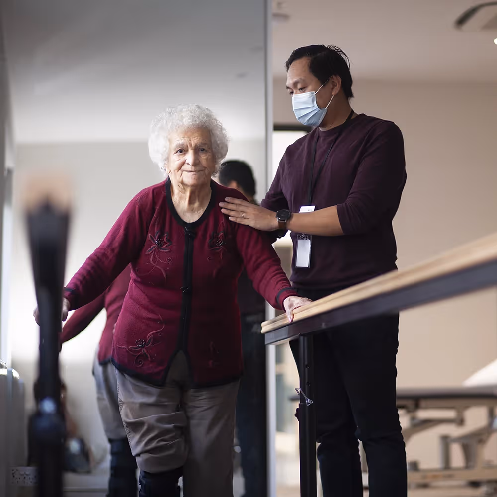Elderly woman receiving mobility support from staff at residential aged care facility near Mill Park.