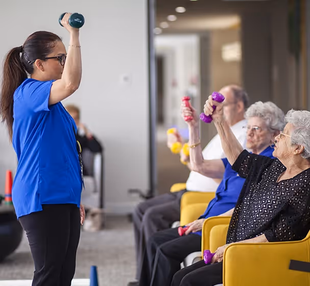 Group of residents in Plenty aged care participating in light-weight exercise guided by staff, promoting health and wellbeing activities.