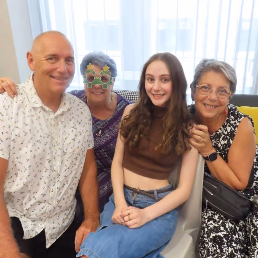 Ida Cinerari, an elderly woman wearing novelty glasses, smiling with three family members during a joyful gathering at Oxa Care.