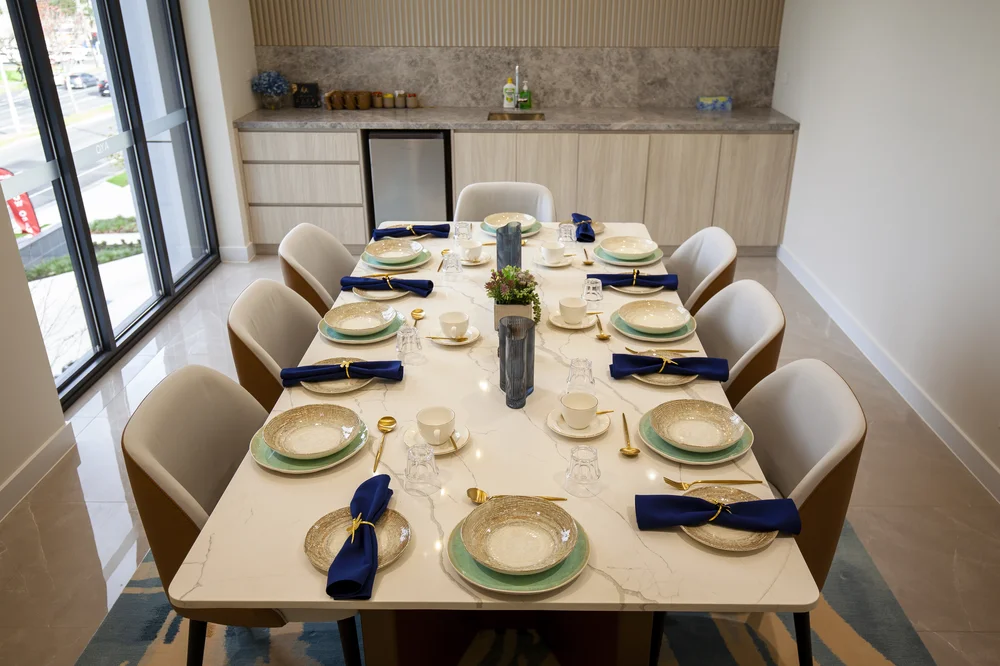 A modern dining room table elegantly set for eight, with plates, cups, gold cutlery, and navy blue napkins neatly arranged, ready for a meal