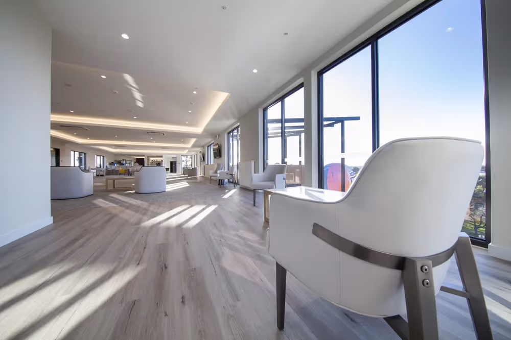 Spacious and modern lounge area with large windows, natural light, wooden flooring, and comfortable seating.