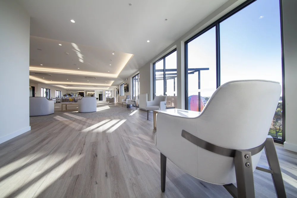 Spacious and modern lounge area with large windows, natural light, wooden flooring, and comfortable seating.