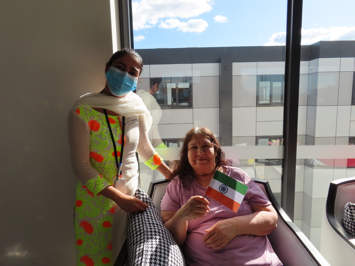 Smiling woman seated indoors holding an Indian flag, with a staff member.