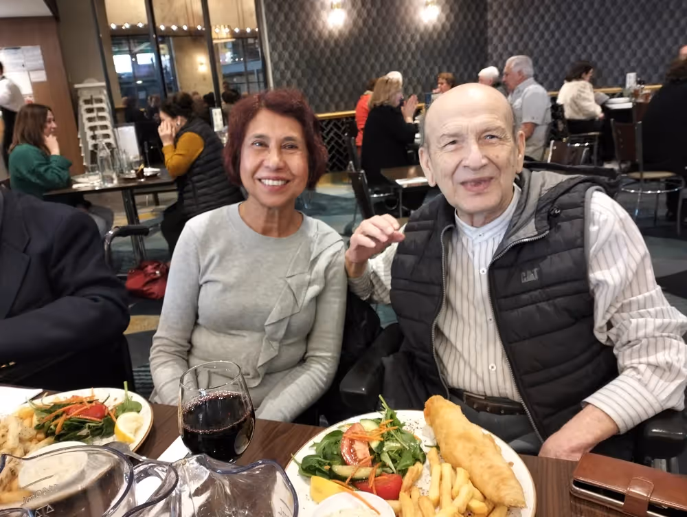 Two elderly people smiling at a dining table in a restaurant setting.