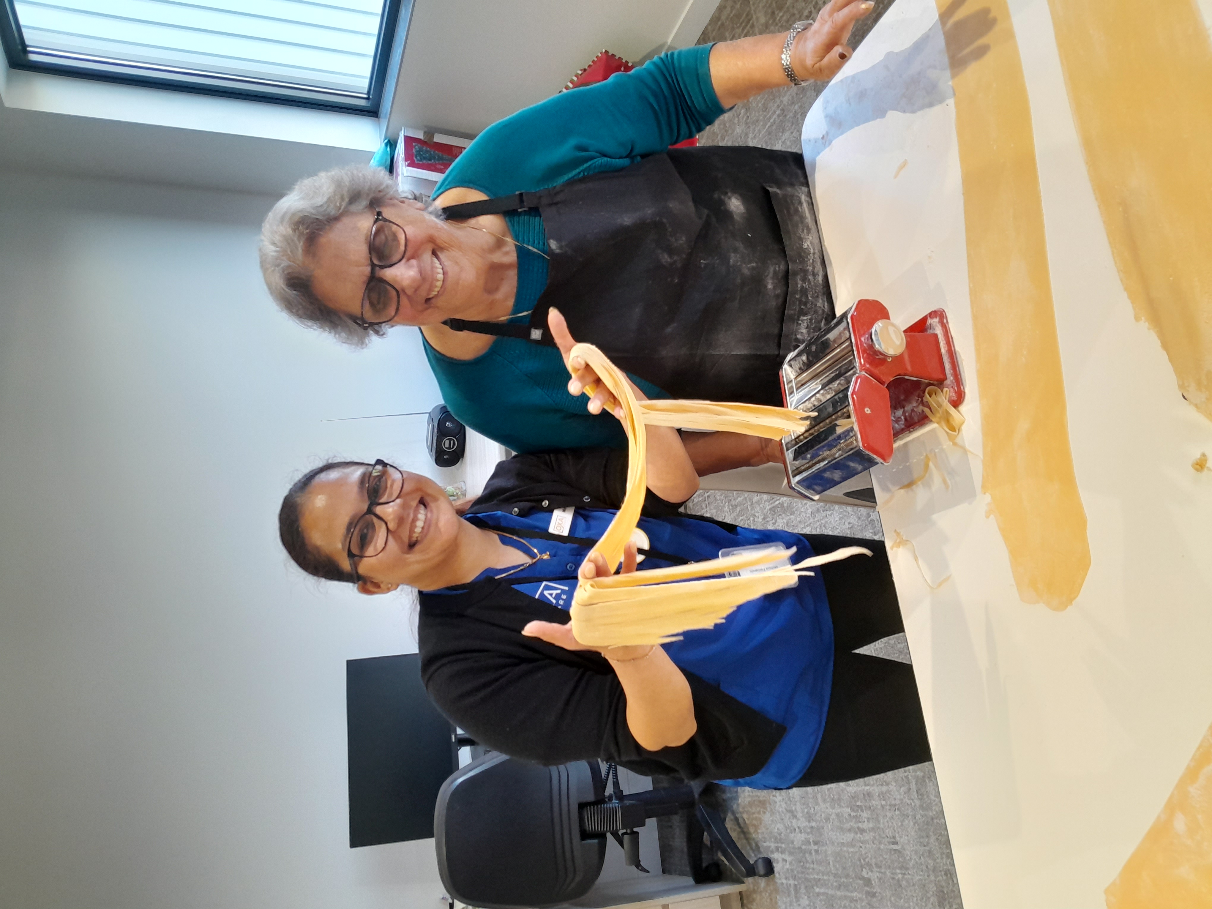 A smiling aged care resident and a staff member making fresh pasta together with a pasta machine.