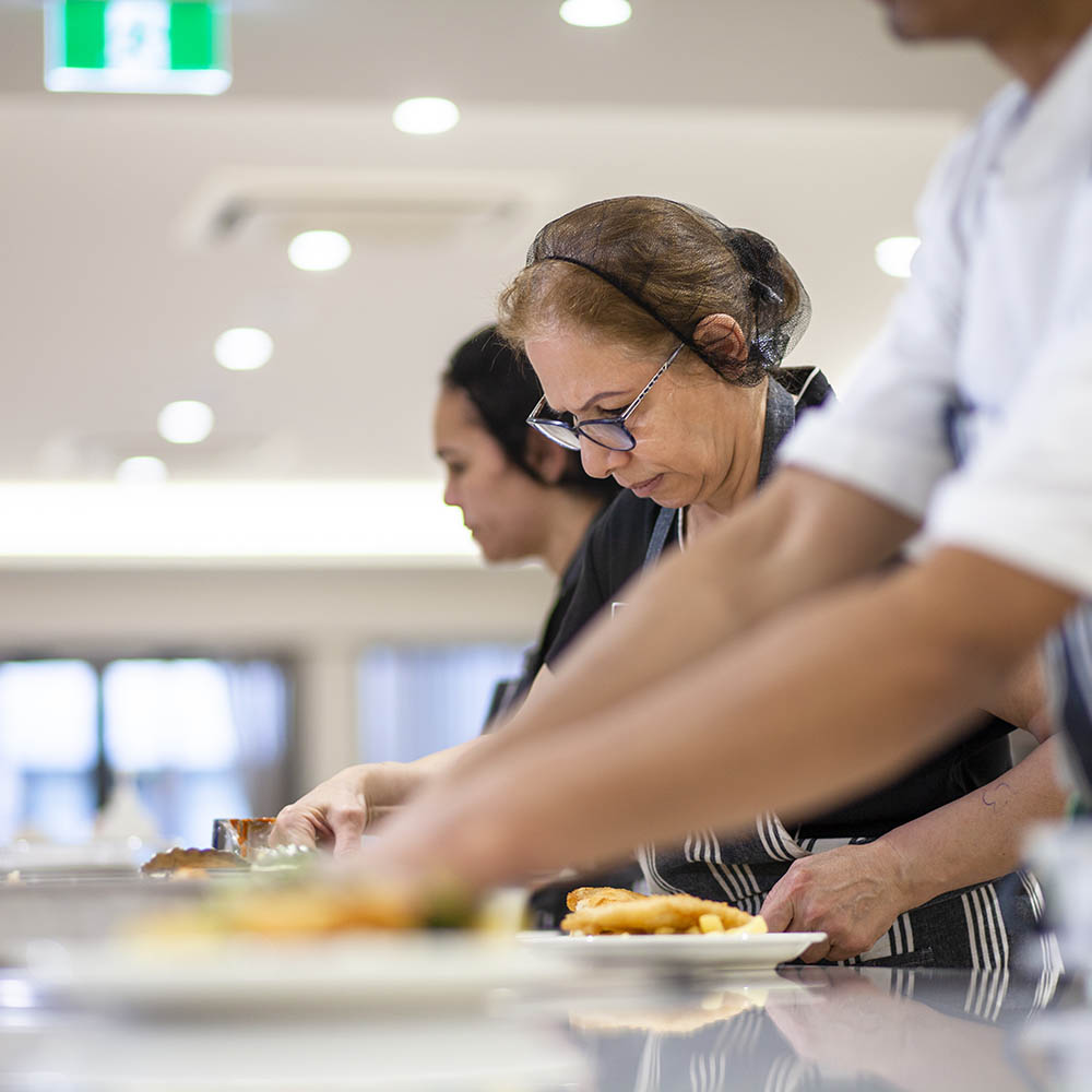 Kitchen team plating fresh meals in a commercial kitchen within a residential aged care facility.