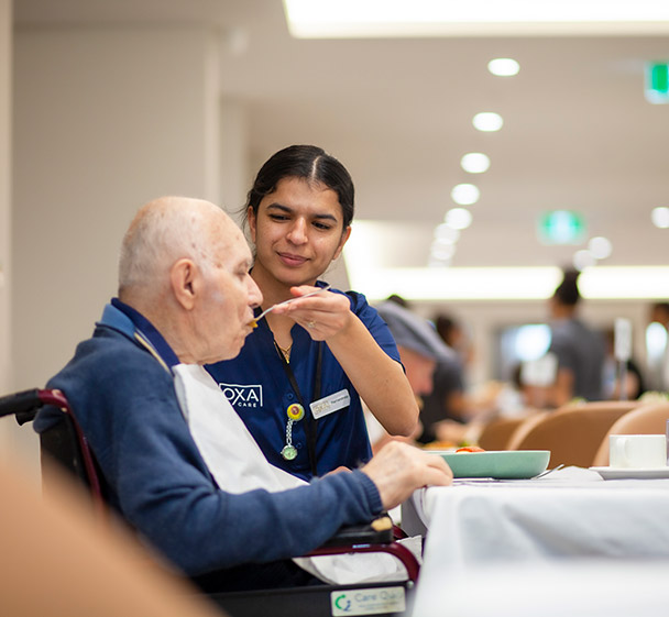 Resident participating in light exercise with a resistance band in a comfortable lounge space.