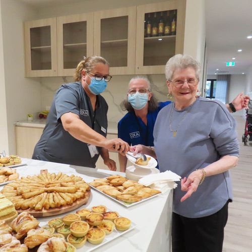 Care staff assisting a resident during a shared afternoon tea in a communal space.