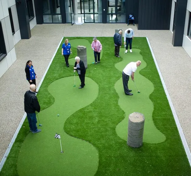 A group of people taking part in a friendly putting game within an open courtyard space.