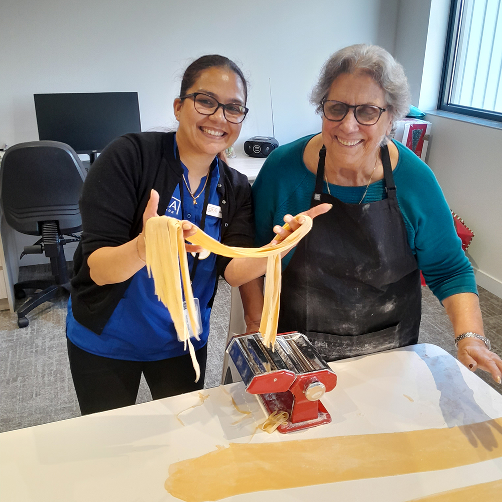 Resident and staff member smiling while making fresh pasta together during a cooking activity.