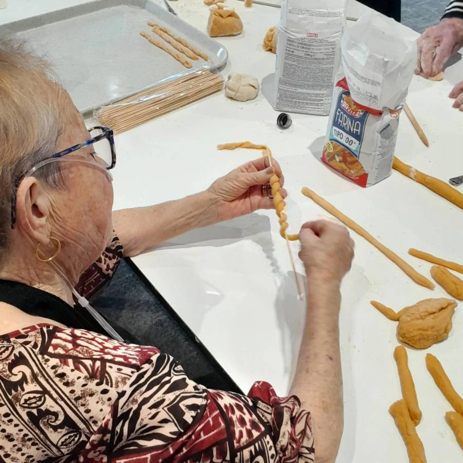 Resident and staff member smiling while making fresh pasta together during a cooking activity.