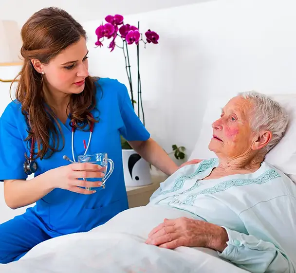 Nurse assisting an elderly resident with a drink while providing bedside care.