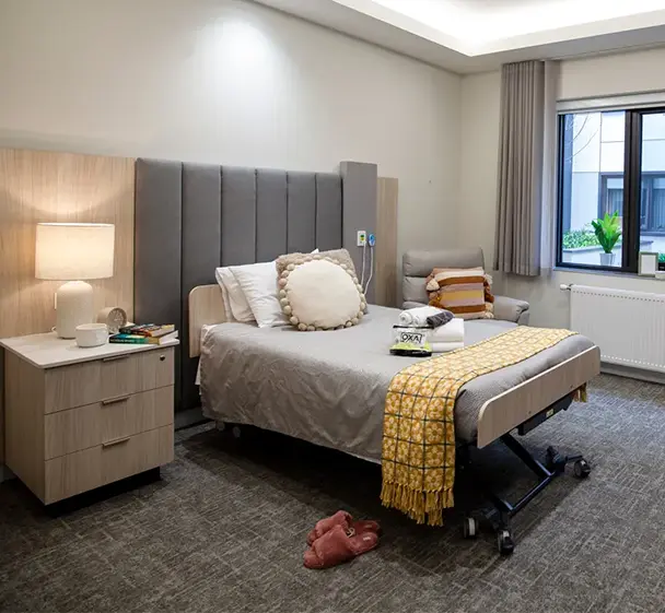 Spacious private aged care room with modern furnishings, electric bed, ensuite bathroom and comfortable seating.