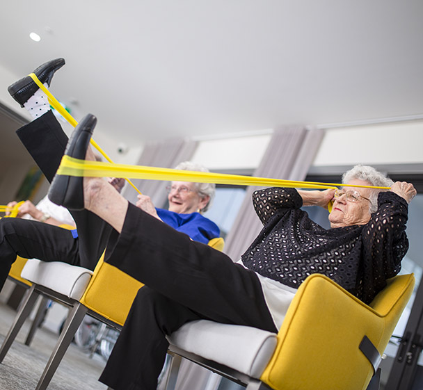 Resident participating in light exercise with a resistance band in a comfortable lounge space.