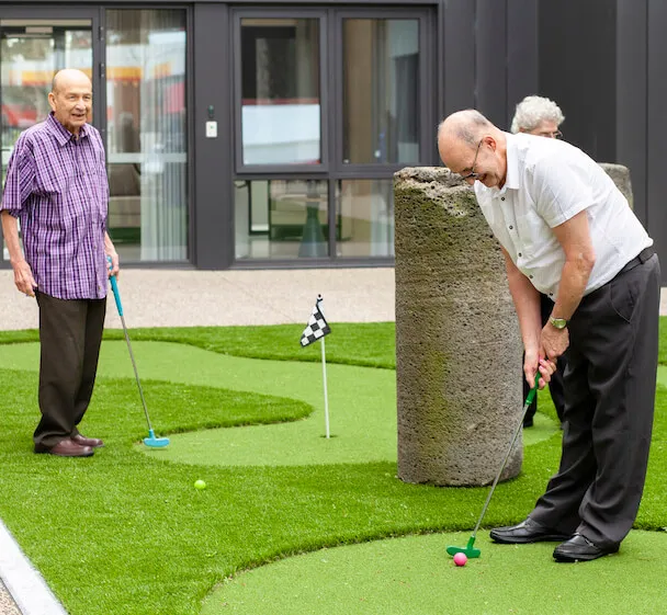 Residents enjoying outdoor leisure activities in a landscaped courtyard within a supportive care community.