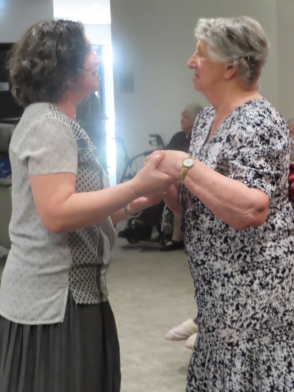 Two aged care residents holding hands and sharing a gentle moment during a social activity.