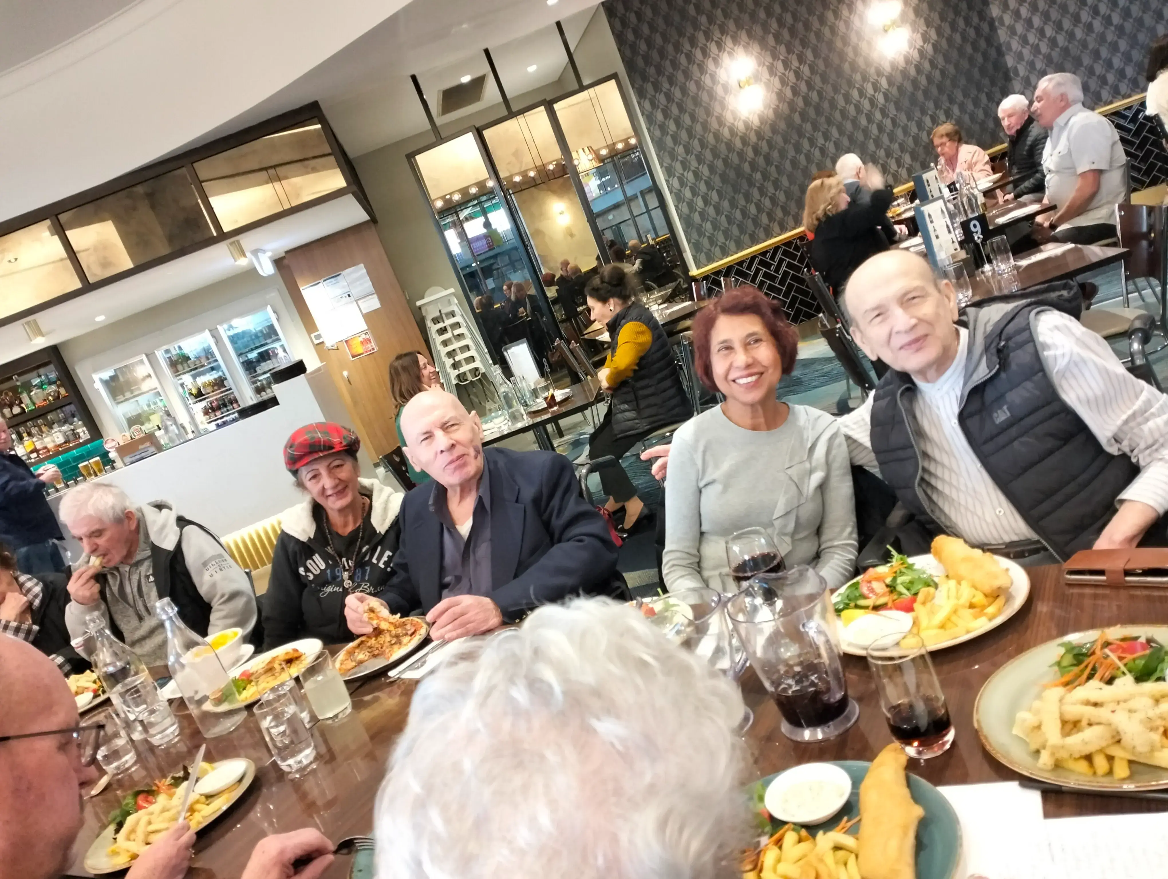 A group of older adults dining together at a long table in a lively restaurant-style setting.