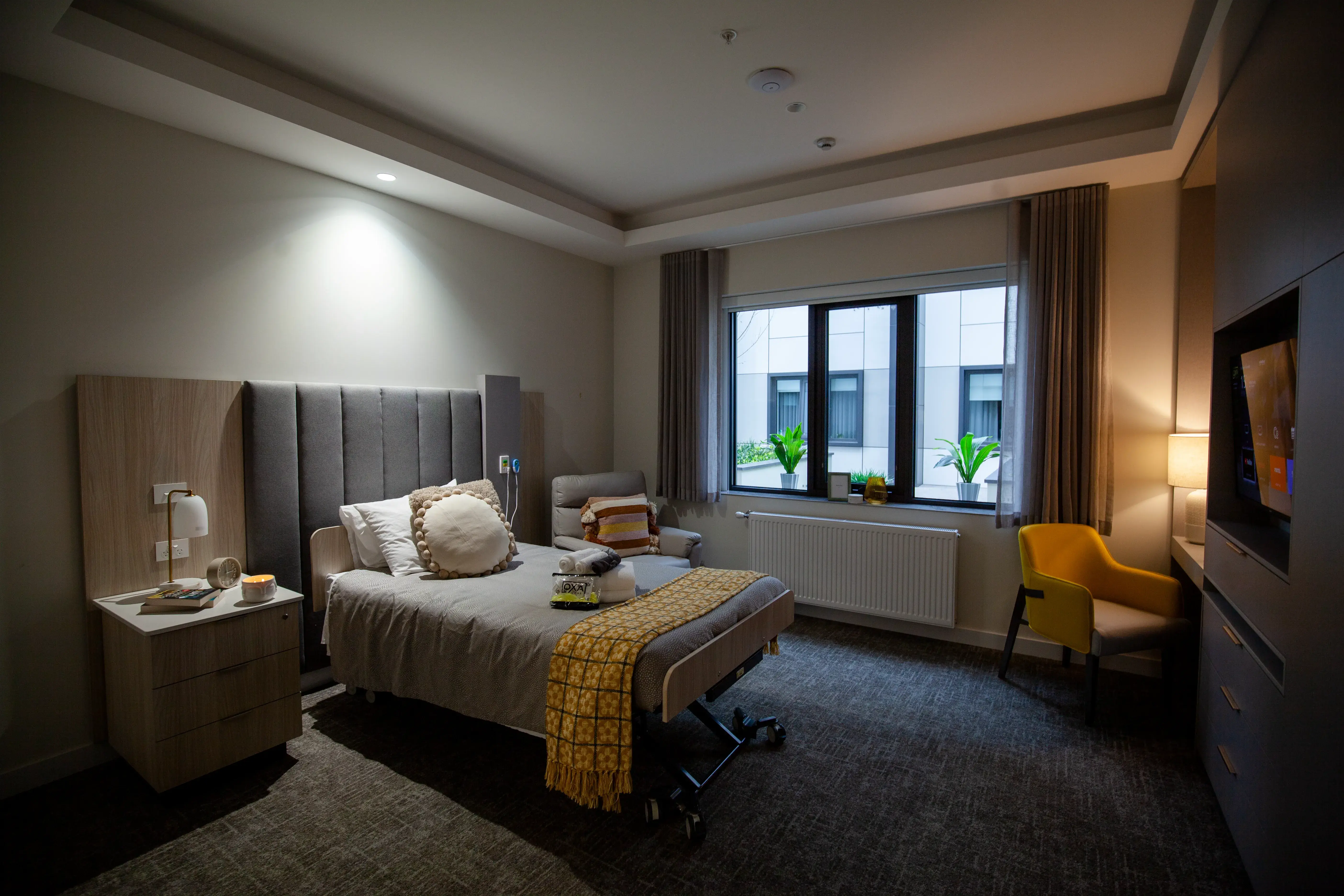 A neatly arranged private bedroom featuring a bed, armchair, and soft lighting.