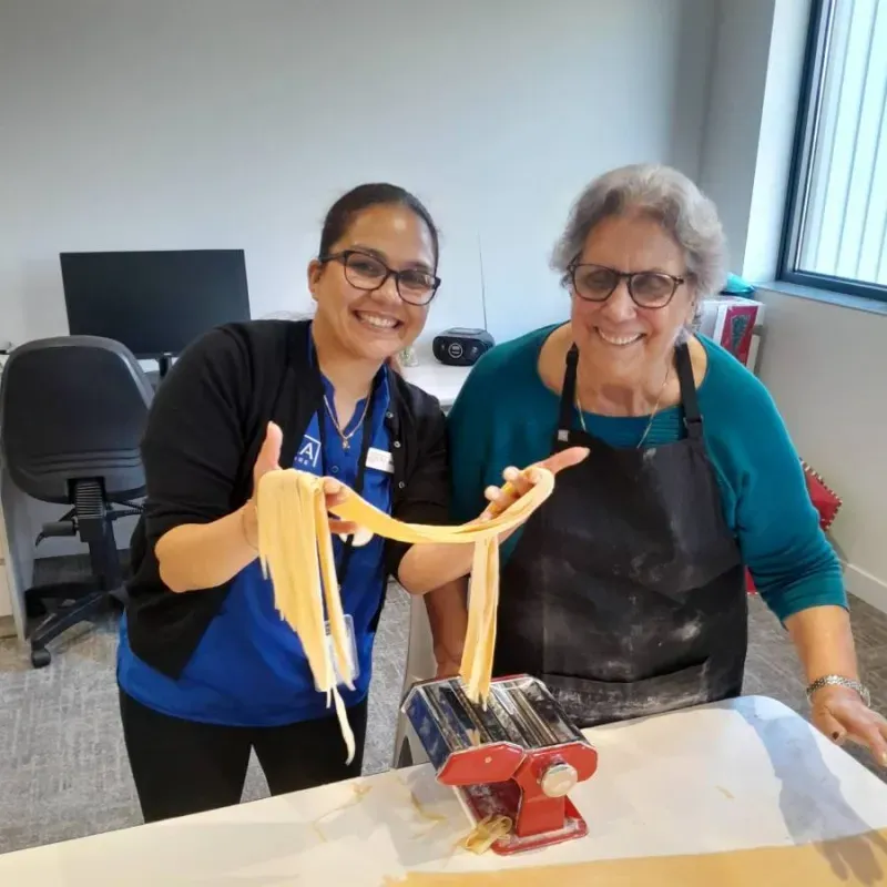 Resident and care team member making fresh pasta together during a hands-on lifestyle activity.