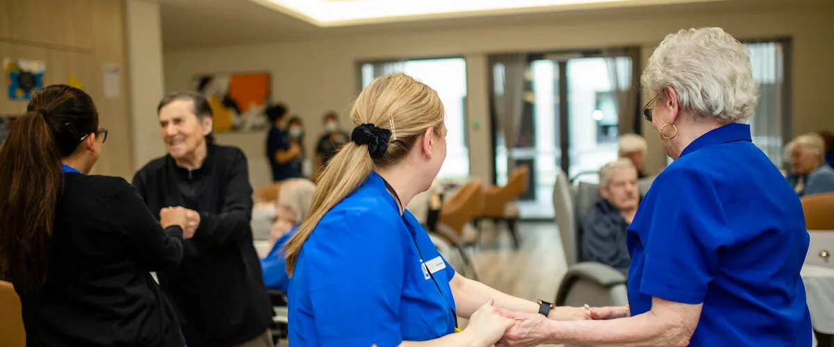Care staff supporting residents during a group social activity in a welcoming environment.
