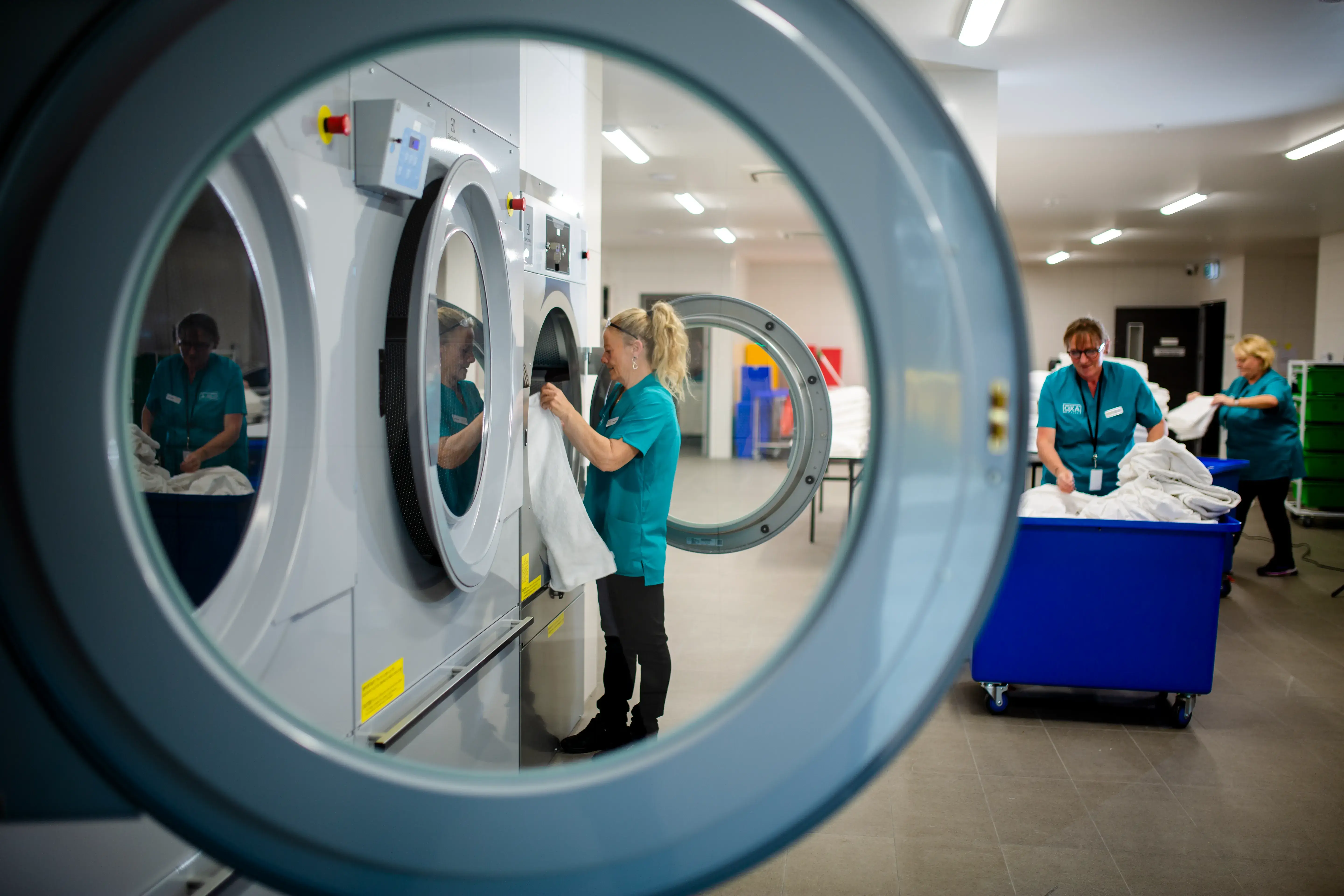 Laundry staff loading clean linens into industrial washing machines in a service area.