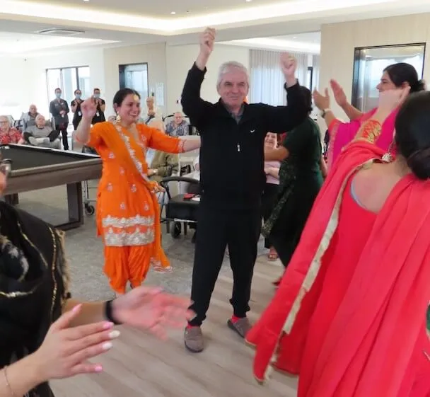 People clapping and dancing together during a lively cultural performance held inside a communal room.