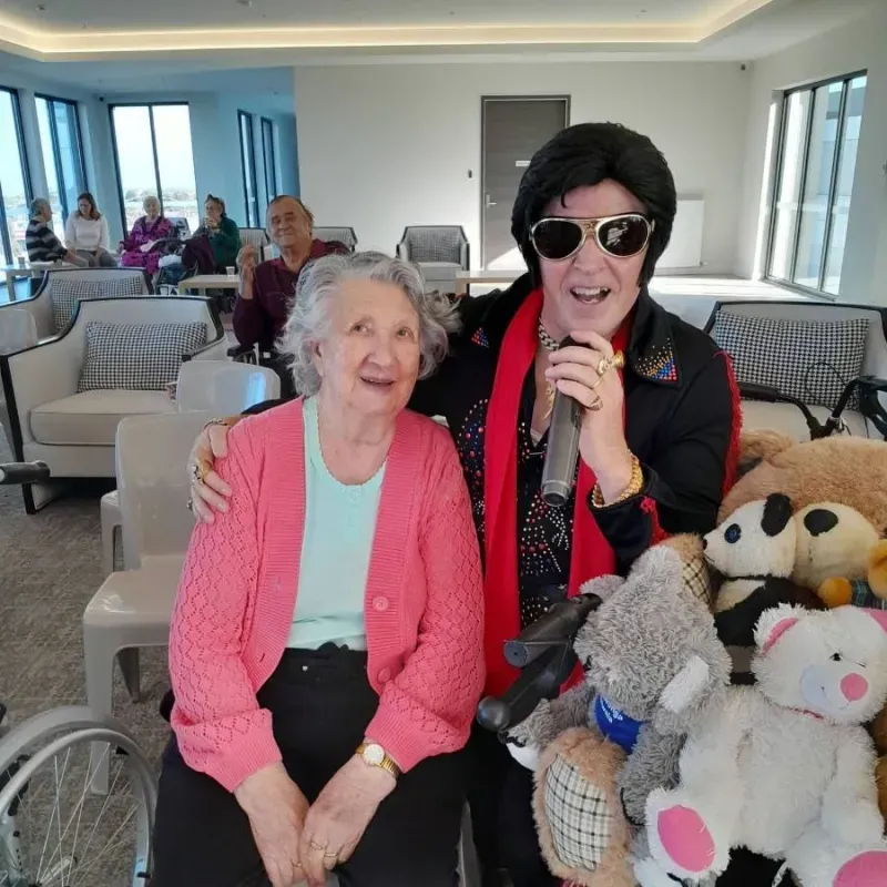 Resident smiling alongside an entertainer during a live performance at Oxa Care.
