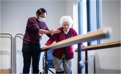 A staff nurse guides a smiling resident during a therapy session in the nursing facility.