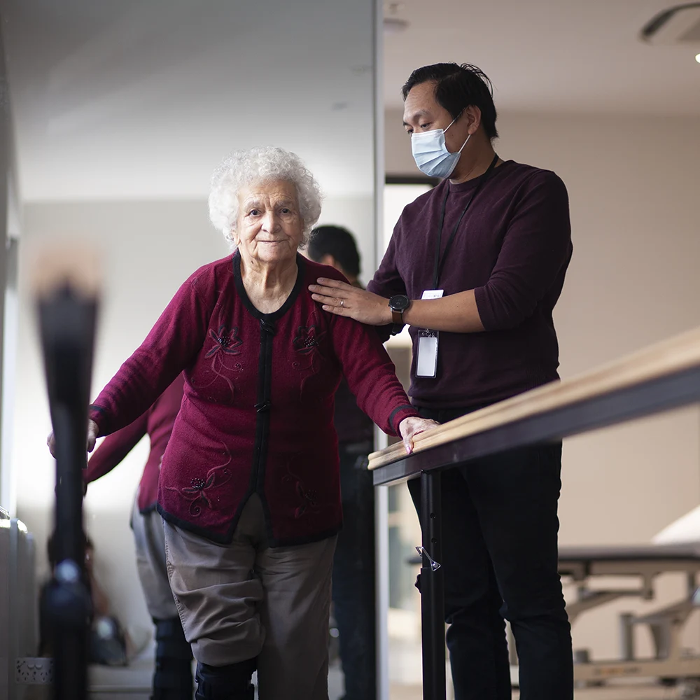 Elderly woman receiving mobility support from staff at residential aged care facility near Carlton