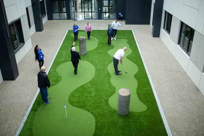 Residents and staff enjoy a game of mini-golf on a professional synthetic putting green in an Oxa Care courtyard.