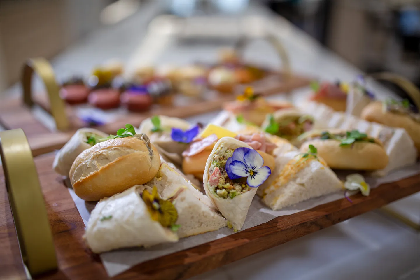 A variety of fresh sandwiches and wraps garnished with edible flowers on a wooden serving tray at Oxa Care.
