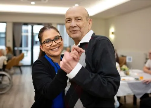 A smiling staff member and an elderly resident share a joyful moment while dancing together at an Oxa Care social event.