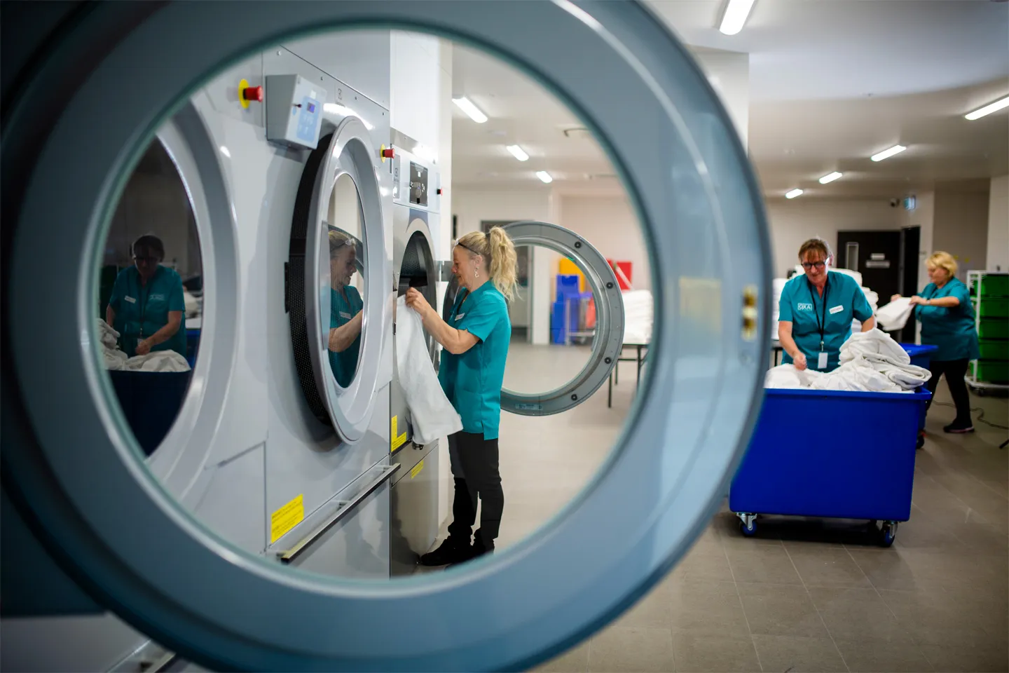 Staff in teal uniforms manage industrial washing and drying machines in the modern, on-site laundry facility at Oxa Care. 