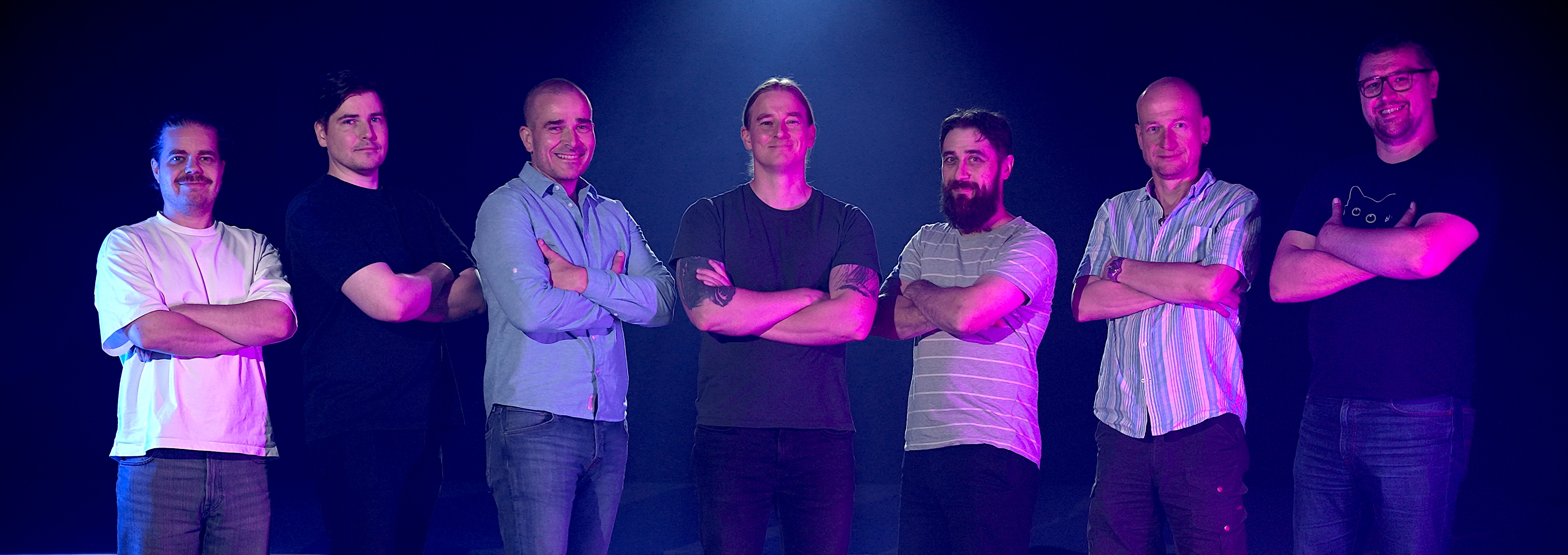 Vallila Studioiden tiimi seisoo rivissä studiossa kädet ristissä sinivioletissa valossa.