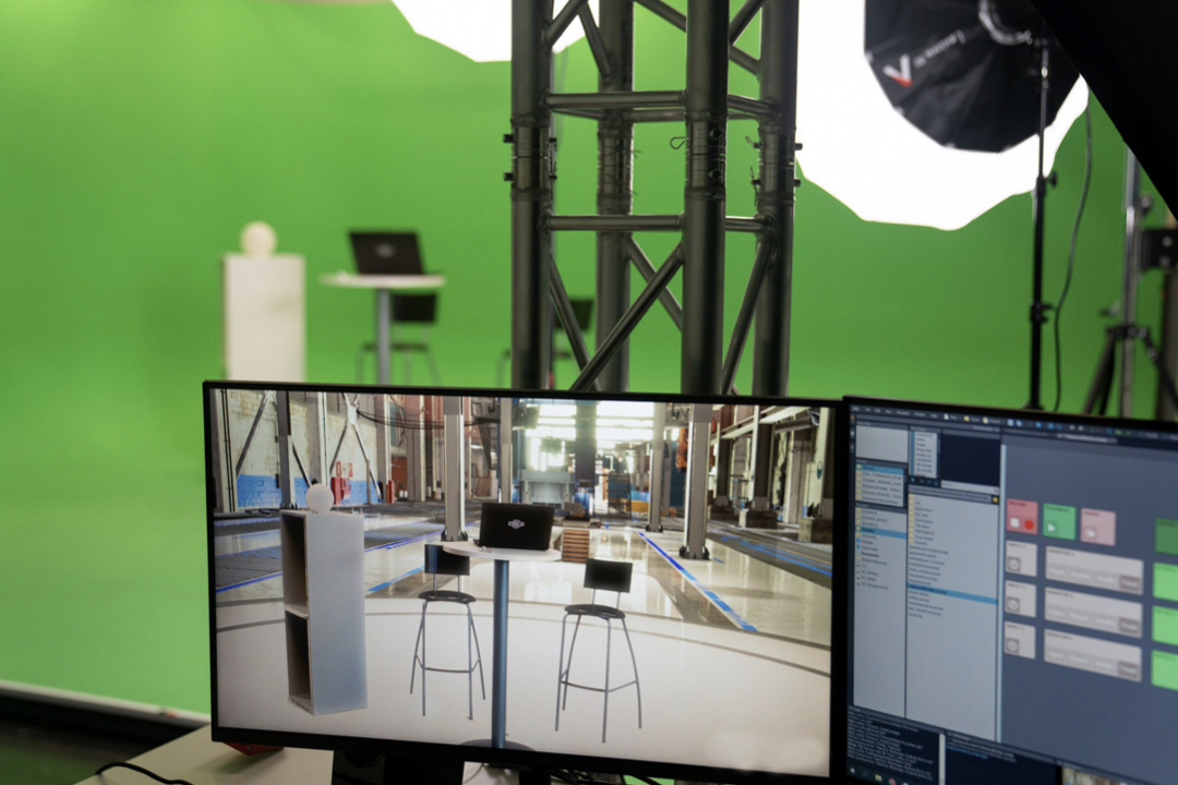 Monitorilla näkyy valmis virtuaalilavastus. Taustalla green screen -studio, jossa kuvaus tehdään.