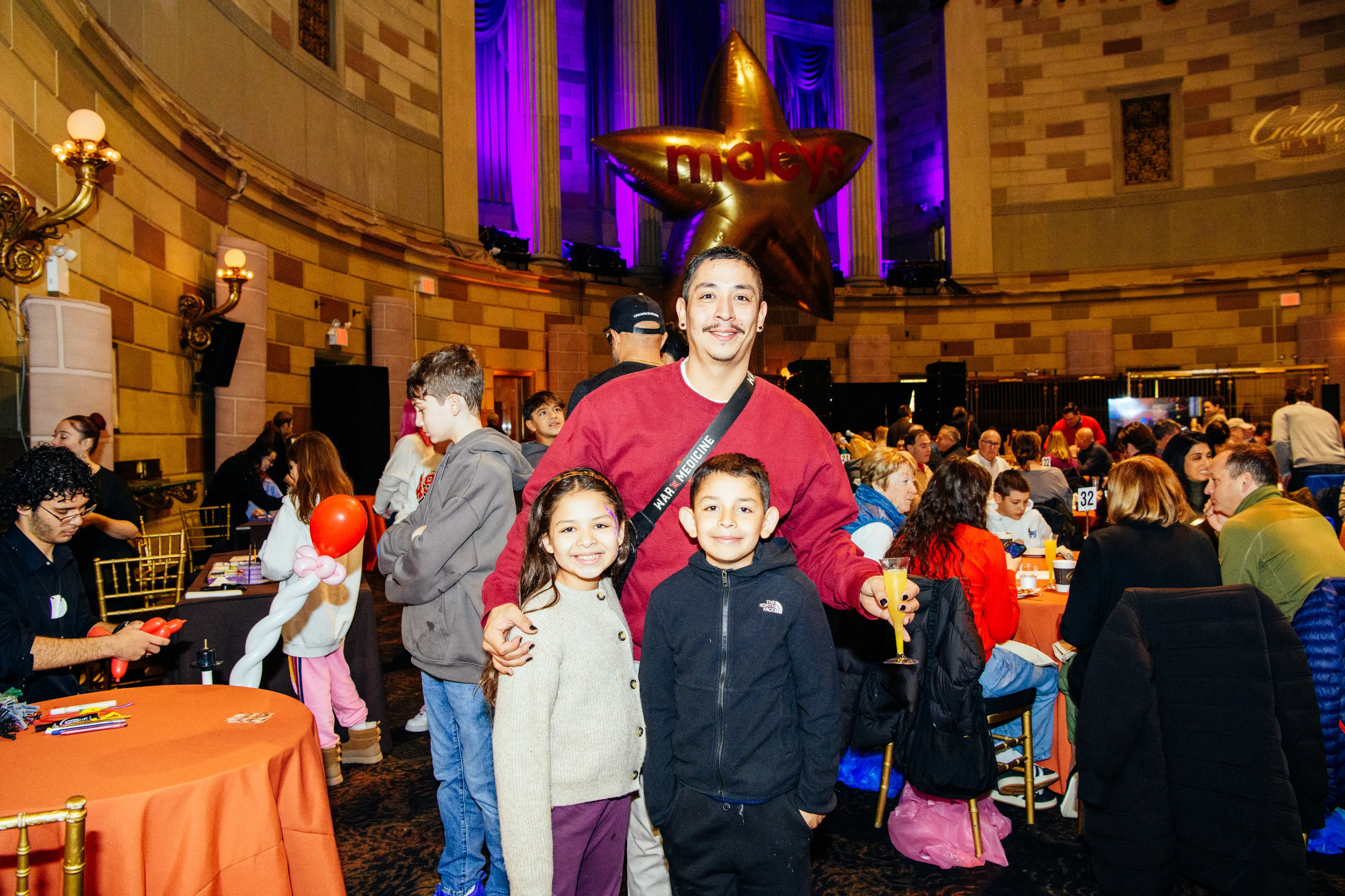Families with kids in the Gotham Hall ballroom under a giant gold star balloon