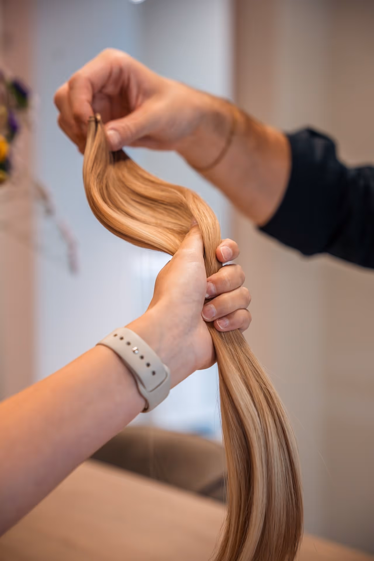 Twee handen die een lange, gladde, blonde haarextensie vasthouden in een kapsalon.