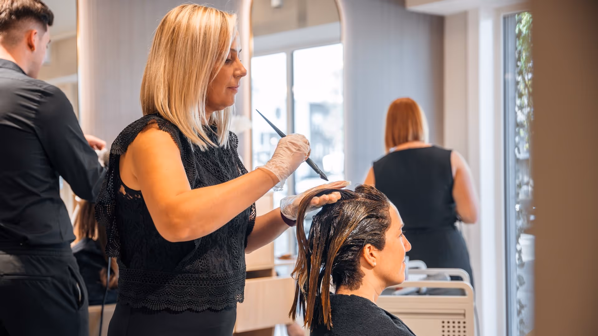 Een kapster brengt haarverf aan op het haar van een klant in een licht, modern salon.